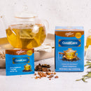 A package of Prince of Peace GoutCare Tea, sachet and ingredients in front of a glass teapot on a table.