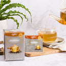 A package of Prince of Peace Immune Tea, a sachet in front of a tea pot pouring Tea on a wood tray.