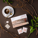 Prince of Peace Organic Black Tea in a tea cup with a package, some tea bags, and tree leaf aside on a brown background.
