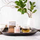A glass of Prince of Peace Organic Black Tea with a package and a teabag on a tray in front of a vase.