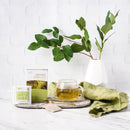 Prince of Peace Organic Green Tea in a cup with a package and some tea bags in front of a vase.
