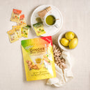 A cup of Ginger Honey Crystal Assorted Matcha on a tablecloth with lemon and ginger, sachets and a package around.
