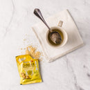 A cup of Prince of Peace Instant Ginger Honey Crystals on a napkin with a opened sachet aside on a white background.
