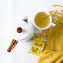 A cup of Prince of Peace Instant Ginger Honey Crystals with a teapot and a sachet next to a yellow blanket.