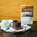 A cup of Prince of Peace Premium Oolong Tea with a wooden teaspoon, teabags, and a package on a table.