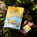 A pachage of Prince of Peace Instant Wild American Ginseng Tea bag and a sachet with a notebook aside lie on the ground in the forest.