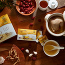 A pot of Chicken soup with Prince of Peace Wild American Ginseng Instant Tea box, sachets and some ingredients like goji, red dates on a table.
