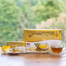 A glass of Prince of Peace Wild American Ginseng Instant Tea with small box, sachet, powder and a package on a desk in a forest.