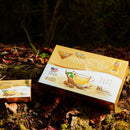 A package of Prince of Peace Wild American Ginseng Instant Tea with an inner box lie on the ground in a forest.