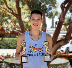 Jeremy Lin in a Tiger Balm shirt holding 2 Telly Award trophies.