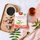 A package of Prince of Peace High Mountain Black Organic Whole Leaf Tea with a cup of tea and tea leaves aside.