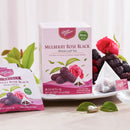 A box of Prince of Peace Mulberry Rose Black whole leaf tea is shown on a white plate with several tea bags, including one unwrapped showing the tea leaves, and loose mulberries and rose petals on a light neutral background.
