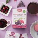 A box of Prince of Peace Mulberry Rose Black Whole Leaf Tea is displayed on a lavender background with styled tea accessories, including a cup of brewed tea, loose dried rosebuds, and mulberries.