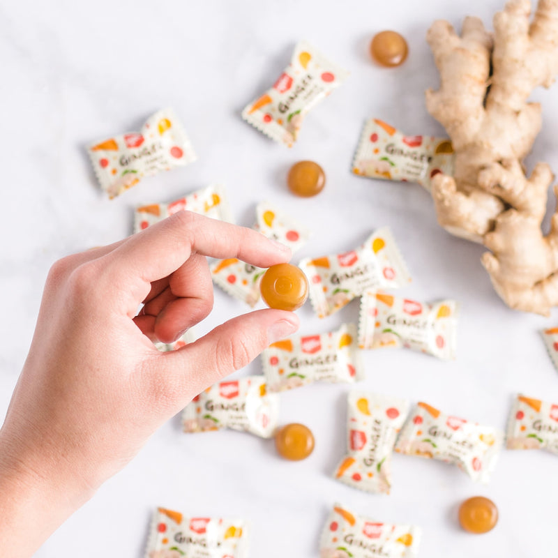 One piece of Prince of Peace Ginger Hard Candy on hand. with some individual wraps and ginger on the white back ground