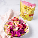 A package of Ginger Chews Lychee aside with some chews, flowers in a white bowl.