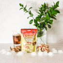 A package of Ginger Chews Cola with ginger root and a glass of iced Cola on a white surface.