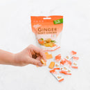 Hand reaching for a Ginger Soft Chews  package with scattered chews on a white background