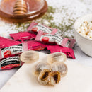 Several wrapped pieces of Honey Loungat Candy are arranged on a white surface, with several translucent hard candies in the foreground and a bowl of popcorn and a wooden honey dipper blurred in the background.