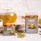 A package of Prince of Peace Immune Tea, a sachet, ingredients around with a teapot on a tray.