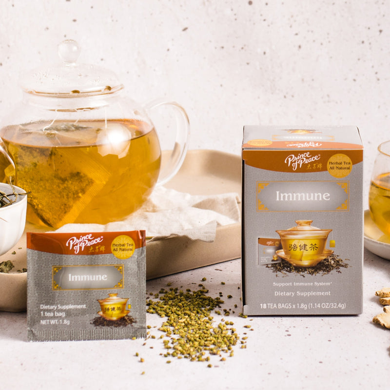 A package of Prince of Peace Immune Tea, a sachet, ingredients around with a teapot on a tray.