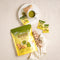 A cup of Prince of Peace Ginger Honey Crystals Matcha with a package, sachets, a ginger and some powder on a tablecloth.