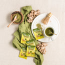 A cup of Prince of Peace Ginger Honey Crystals Matcha and Matcha powder with sachets and gingers on a tablecloth.