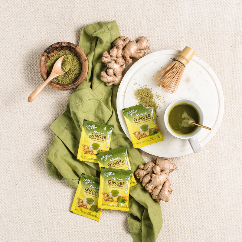 A cup of Prince of Peace Ginger Honey Crystals Matcha and Matcha powder with sachets and gingers on a tablecloth.