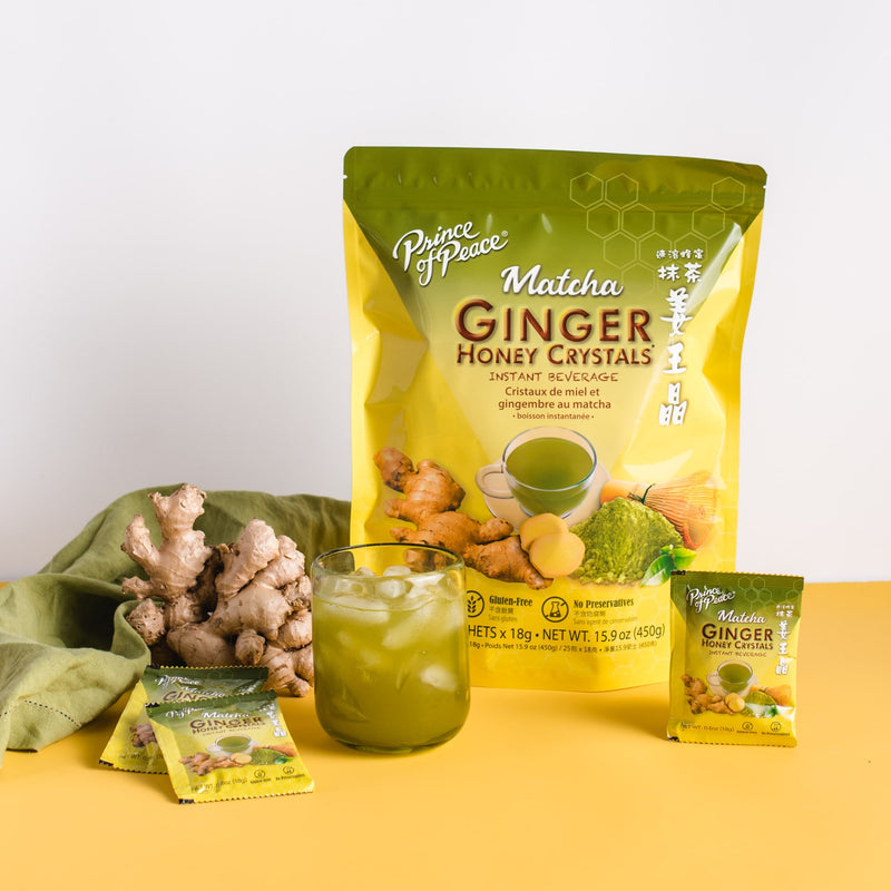 A glass of cold Prince of Peace Ginger Honey Crystals with Matcha with sachets, gingers and package on a able.