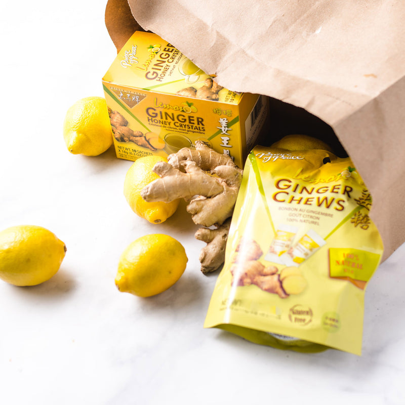 A package of Prince of Peace Ginger Candy (Chews) with Lemon and a box of Ginger Honey Crystal with some lemons and ginger in a paper bag on a white background.