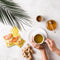 A cup of Prince of Peace Instant Ginger Honey Crystals Turmeric with a honey jar and sachets and ginger aside.