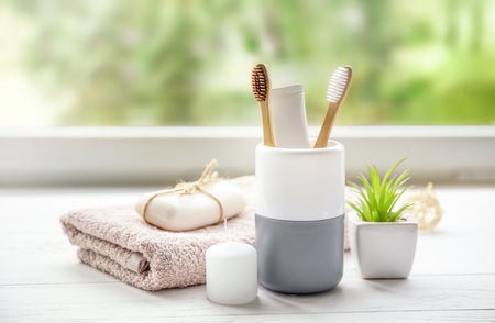 White and gray toothbrush holder with toothbrushes on a windowsill with plants and towels.