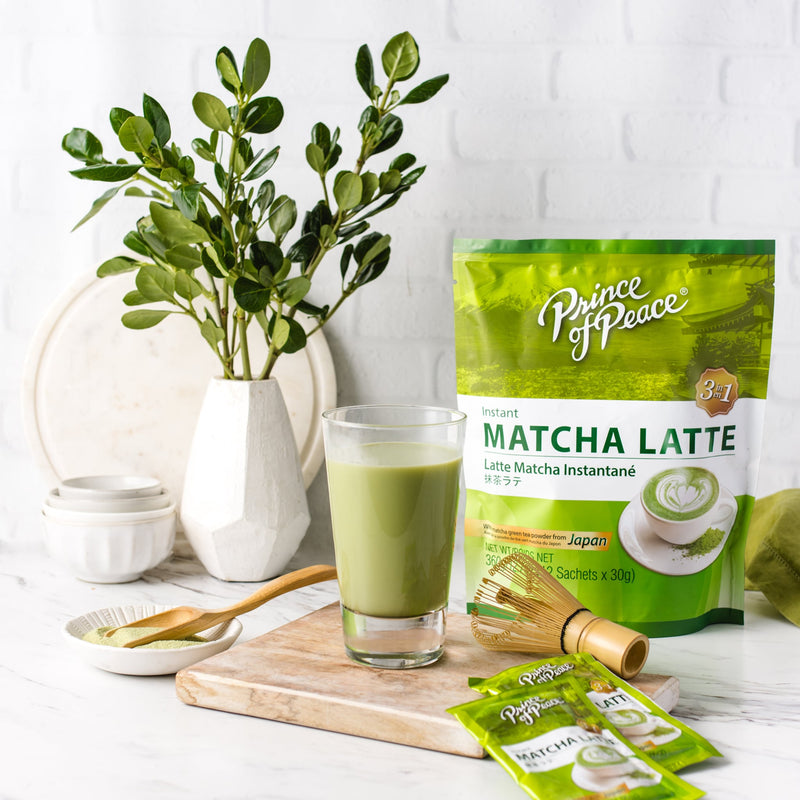 A glass of Prince of Peace 3-in-1 Instant Matcha Latte with matcha powder and plants aside.