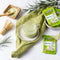 A glass of Prince of Peace 3-in-1 Instant Matcha Latte  and a cup of hot one with matcha powder and sachets aside on a blanket.
