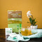 A glass of Prince of Peace Premium Japanese Style Green Tea with teabags, a package and an orchid on a table..