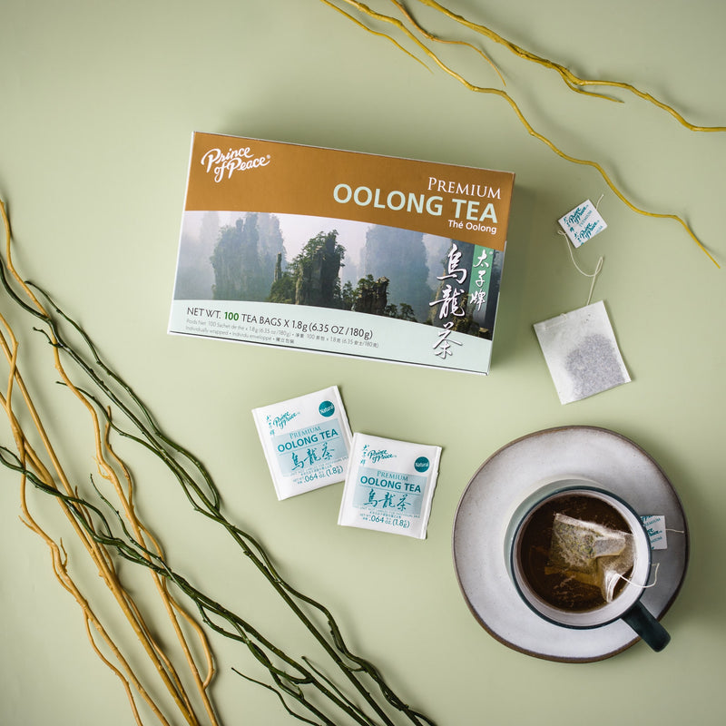 A cup of Prince of Peace Premium Oolong Tea with teabags, a package aside on a green background.