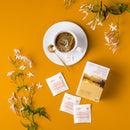 A cup of Prince of Peace Organic Jasmine Green Tea with a package and tea bags, jasmine aside on an orange background.