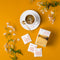 A cup of Prince of Peace Organic Jasmine Green Tea with a package and tea bags, jasmine aside on an orange background.