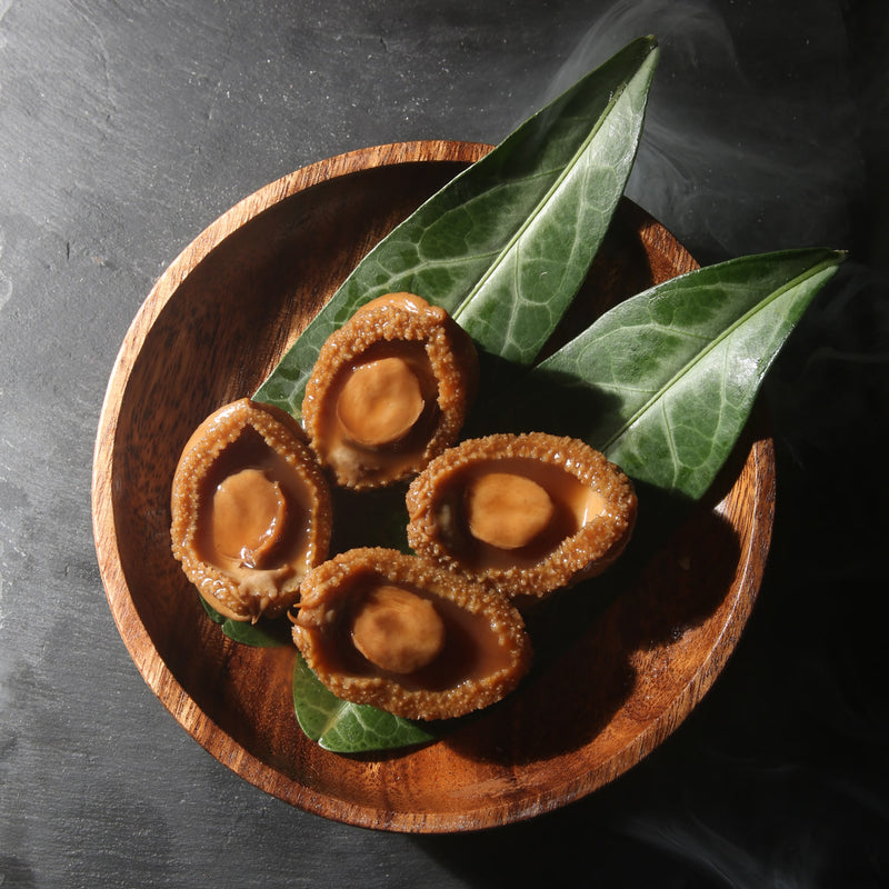 4 pieces of On Kee Braised Abalone on leaves in a wooden tray.
